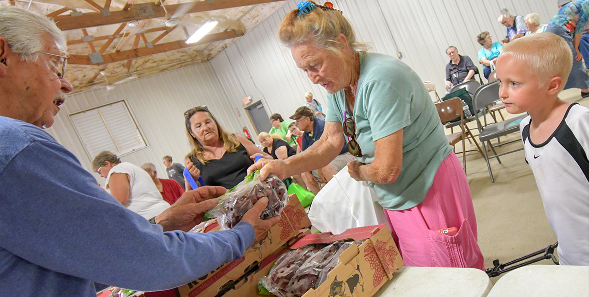 senior man volunteer handing produce to senior woman and grandson at mobile distribution
