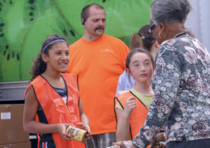 students wearing orange vests girls volunteering and handing cans to senior woman at care mobile