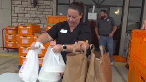 A woman sets out grocery orders on a table for patients to pick up at distribution.